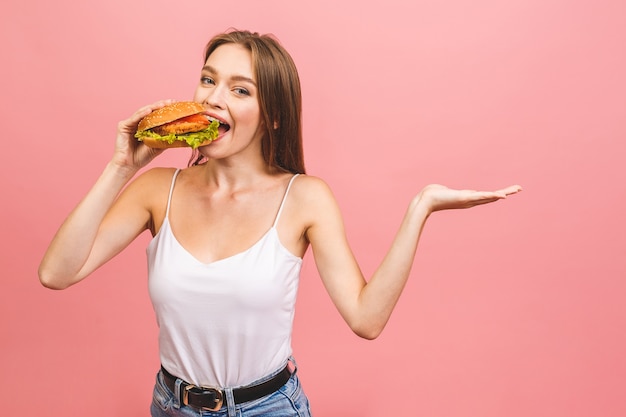 Portrait of young beautiful hungry woman eating burger