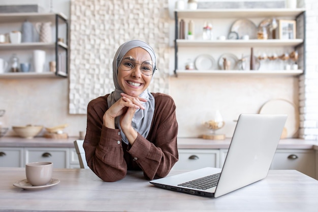 Portrait of a young beautiful muslim female student in a hijab studying remotely on a laptop smiling