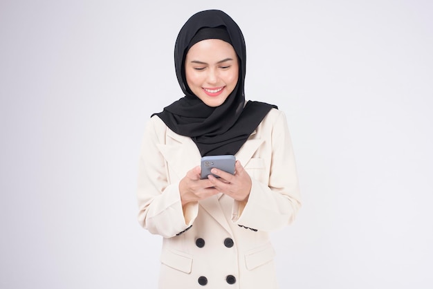 Portrait of young beautiful muslim woman in suit using smart phone over white background