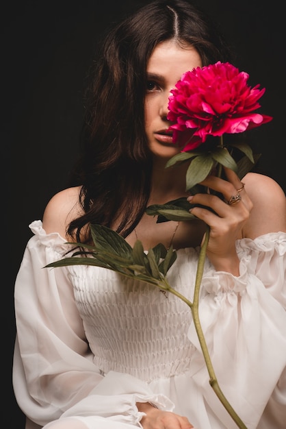 Portrait of a young, beautiful and sensual woman with 1 red peony flower in her hands