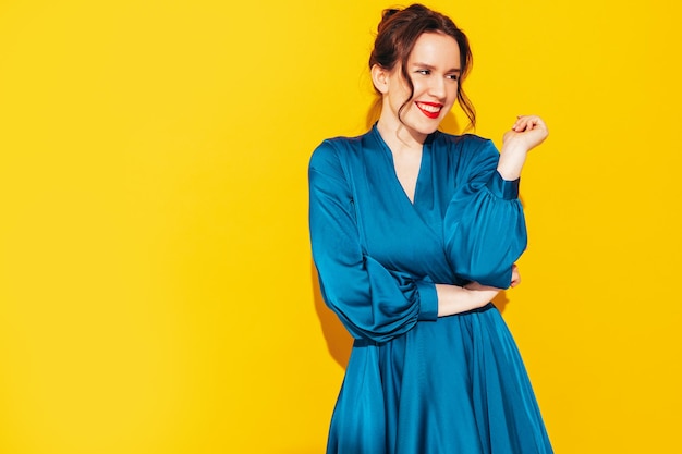 Portrait of young beautiful smiling female in trendy summer blue dress Sexy carefree woman posing near yellow wall in studio Positive model having fun and going crazy Cheerful and happy