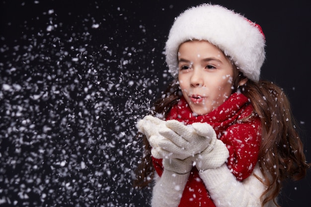 Portrait of young beautiful smiling girl in red Santa hat on a dark background