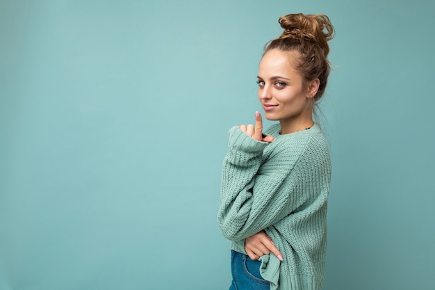 Portrait of young beautiful smiling hipster woman in trendy outfit. Sexy carefree female person posing isolated near blue wall in studio with free space. Positive model with natural makeup.