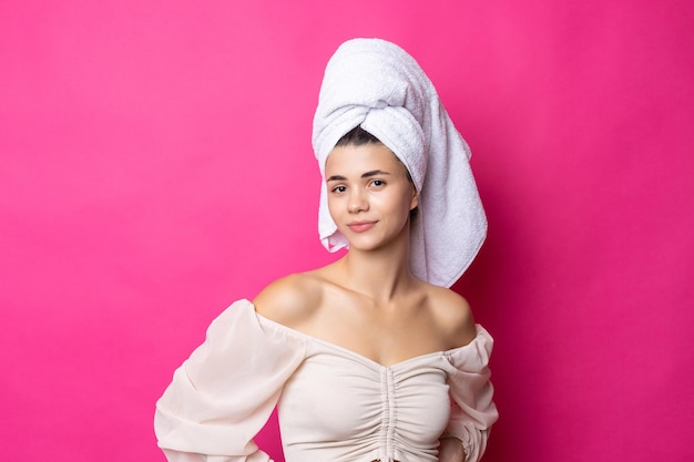 Portrait of young beautiful woman after bath Beauty face of a cheerful attractive girl with towel on head against a pink background