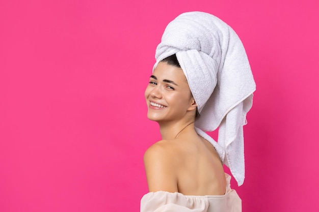 Portrait of young beautiful woman after bath Beauty face of a cheerful attractive girl with towel on head against a pink background