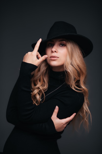 Portrait of a young beautiful woman in black hat on black wall