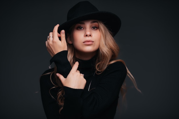 Portrait of a young beautiful woman in black hat on black wall