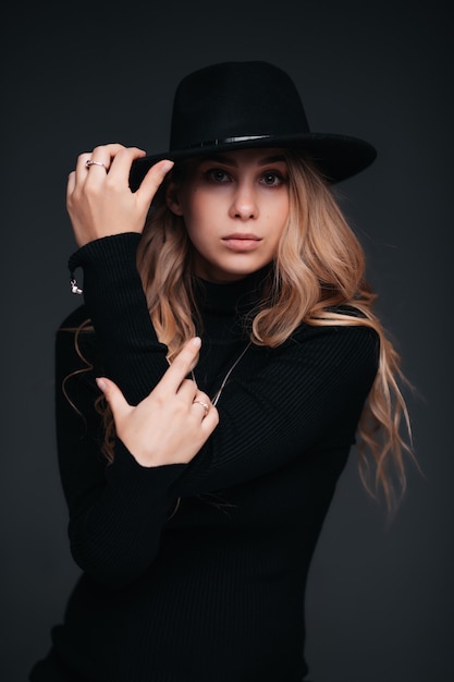 Portrait of a young beautiful woman in black hat on black wall