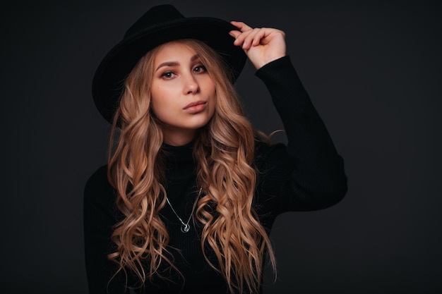 Portrait of a young beautiful woman in black hat on black wall