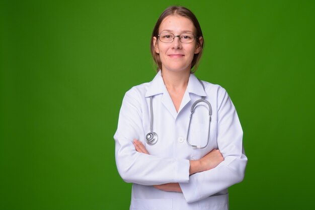 Portrait of young beautiful woman doctor against green wall