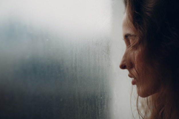 Portrait of young beautiful woman in profile near misted window