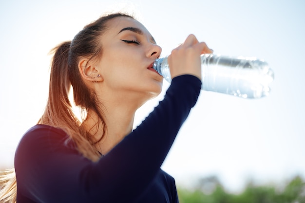 Portrait of young beautiful woman wearing blue sportswear drinking water at park