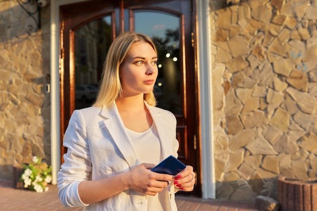 Portrait of young beautiful woman in white jacket looking to side in sunset