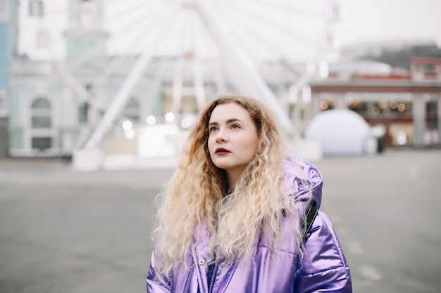 Portrait of young beautiful woman with curly blondie hair outdoors. Beauty, fashion concept. Street style. Bokeh background