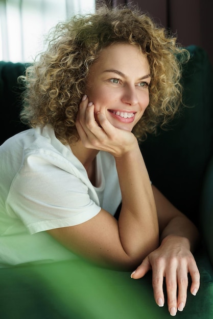 Portrait of young and beautiful woman with curly hair lying on green sofa