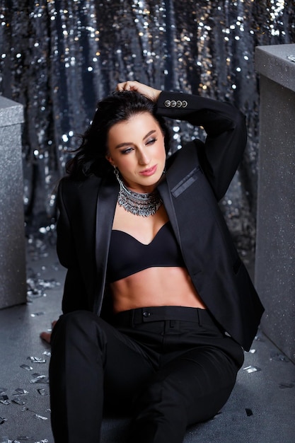 Portrait of a young beautiful woman with dark hair of European appearance Dressed in a black jacket Silver shiny background