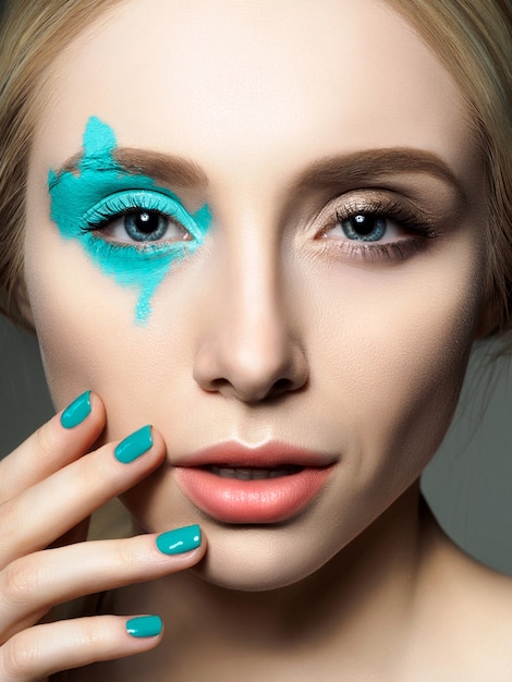 Portrait of young beautiful woman with fashion make up touching her face. Model posing over gray background. 