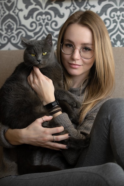 Portrait of a young beautiful woman with her gray cat with bright yellow eyes