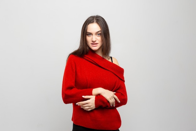 Portrait of a young beautiful woman with a light smile dressed in a red sweater on a light gray background