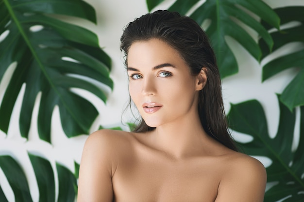 Portrait of young and beautiful woman with perfect smooth skin in tropical leaves