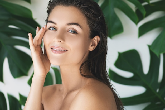 Portrait of young and beautiful woman with perfect smooth skin in tropical leaves