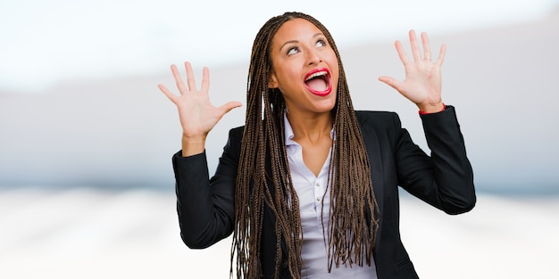 Portrait of a young black business woman screaming happy, surprised by an offer or a promotion, gaping, jumping and proud