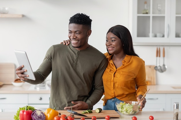 Portrait of young black couple with digital tablet posing in kitchen interior