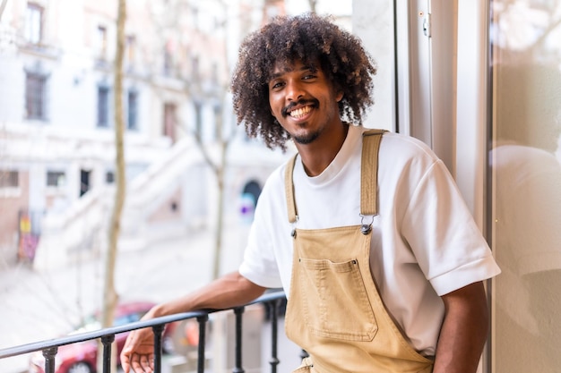 Portrait of a young black ethnic man on a balcony at home everyday situation apartment smiling