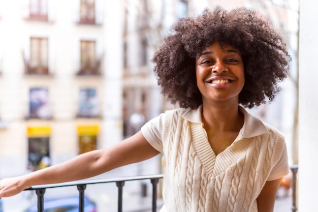 Portrait of a young black ethnic woman with afro hair on a balcony at home smiling everyday situation apartment