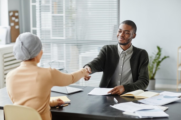 Portrait of young black man shaking hands with female hr manager after successful job interview in o