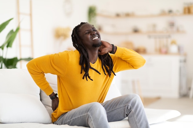 Portrait Of Young Black Man Suffering Neck And Back Pain At Home