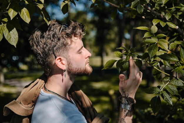 Portrait of a young blond man smelling some green leaves in a park in spring