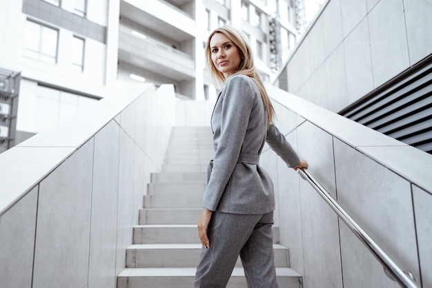 Portrait of young blonde businesswoman in gray suit walking in the city