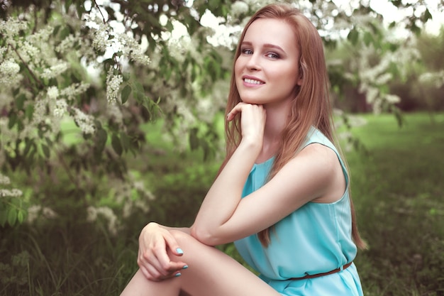 Portrait of a young blonde girl in a blue dress. trees in flowers.