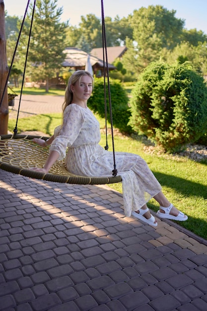 Photo portrait of a young blonde woman in a pastel chiffon dress circling in a wicker hammock