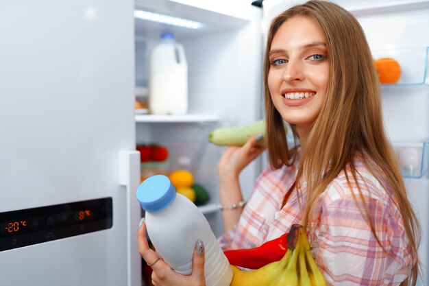 Portrait of a young blonde woman taking food from her fridge