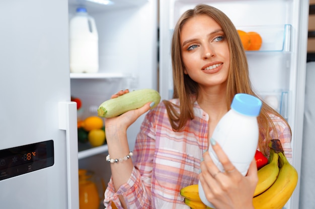 Portrait of a young blonde woman taking food from her fridge