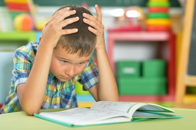 Portrait of young boy reading book in classroom