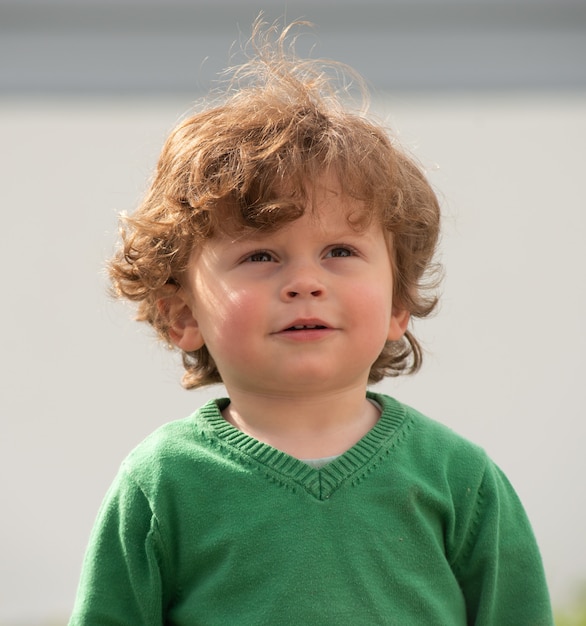 Portrait of young boy with green sweater playing outdoors