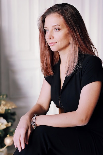 Portrait of a young brunette girl with a beautiful smile, long hair in black clothes