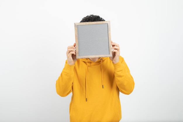 Portrait of a young brunette man standing and covering face with gray frame .