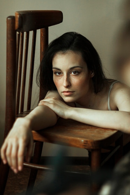 Portrait of a young brunette in a room who is leaning on a wooden chair