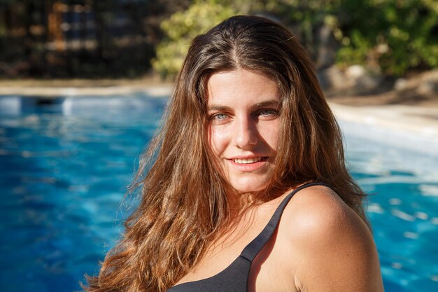 Portrait of young brunette smiling happily at camera posing on pool