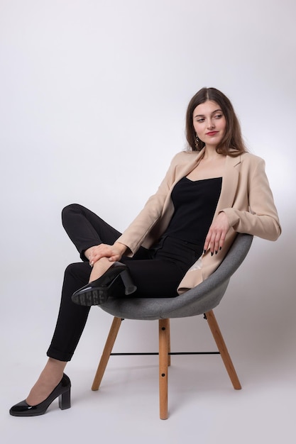 Portrait of a young brunette with long hair in the studio Cute girl sitting on a chair on a white background