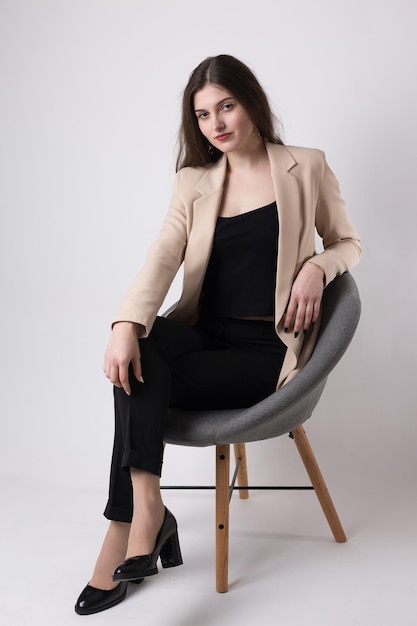 Portrait of a young brunette with long hair in the studio Cute girl sitting on a chair on a white background