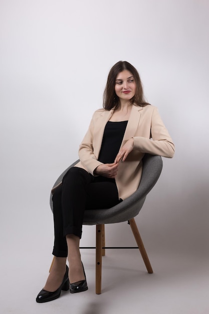 Portrait of a young brunette with long hair in the studio Cute girl sitting on a chair on a white background