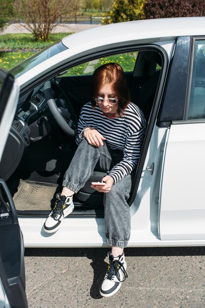 Photo portrait of a young brunette woman driving in a car using a smartphone