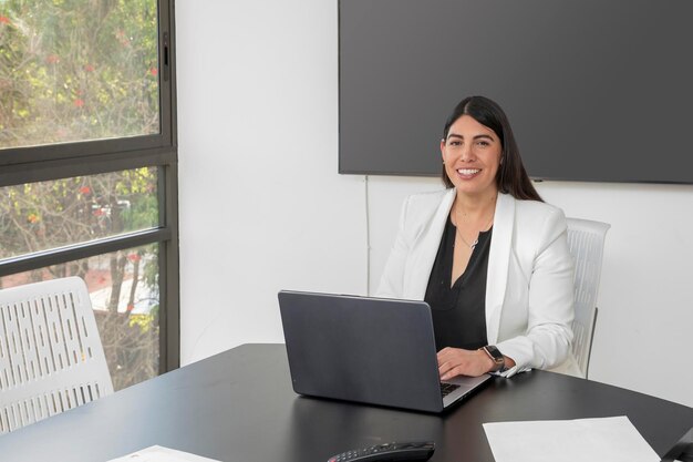 Portrait of a young business woman looking at the camera in her office while working on her laptop