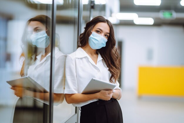 Portrait of young business woman in protective face mask an office building hallway.