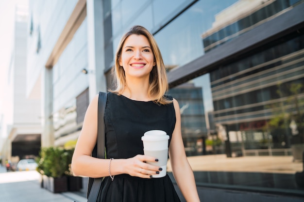 Portrait of young business woman walking to work while drinking takeaway coffee